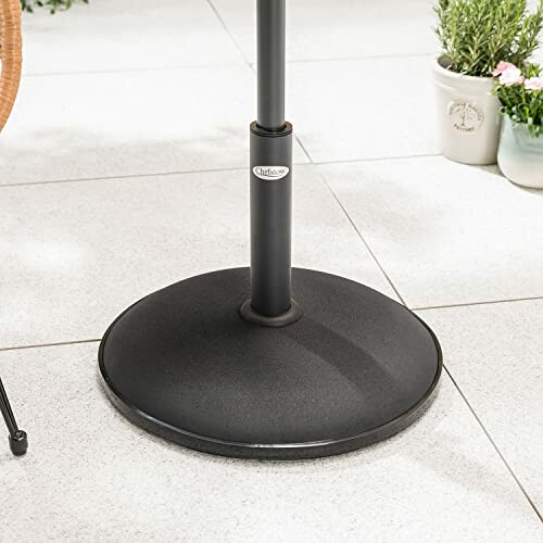 Black umbrella base on tiled patio with plants.